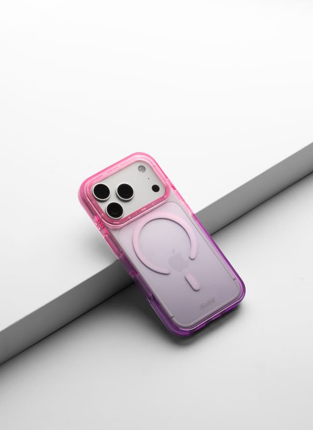 CLICK Clear Ombre MagSafe case in a pink-to-purple gradient with MagSafe ring, shown at an angle against a white and gray backdrop