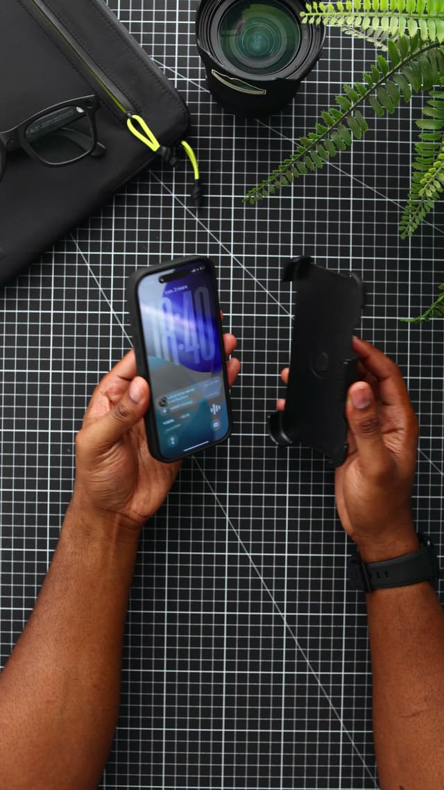 An iPhone 17 Pro in a black CLICK Latch Holster case held in one hand, and the empty belt-clip holster held clip-out in the other