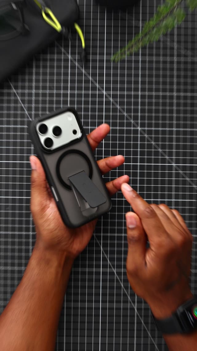 Two hands holding an iPhone 17 Pro in a black CLICK Latch Holster case with the kickstand swung out of the magnet ring